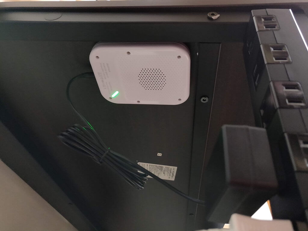 机の裏に貼り付けたdeskHackに、AC電源をつないだ様子。緑のLEDが点灯する